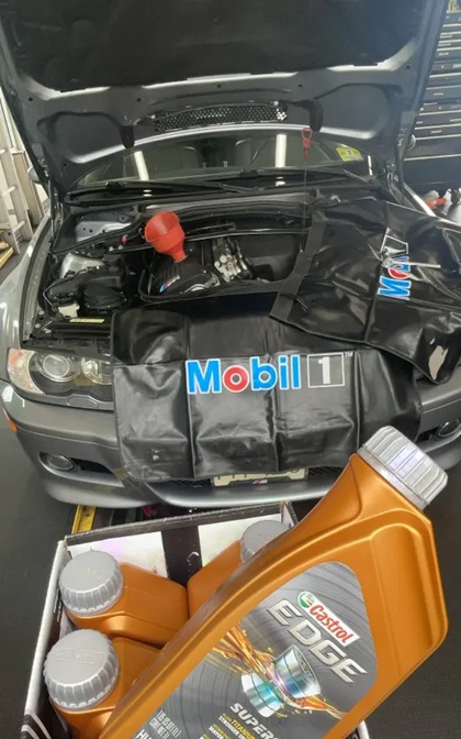Silver BMW M3 with hood open and a Mobil 1 fender cover in place during a Castrol EDGE full synthetic oil change.